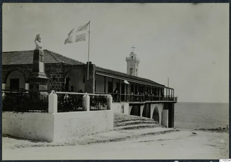 Monastery building on the seafront with a flag, a cross and a bust on a pedestal