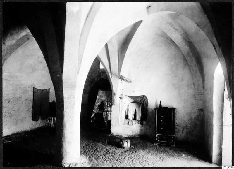 Vaulted interior of a monastery building with a dark wooden cupboard and hanging cloths