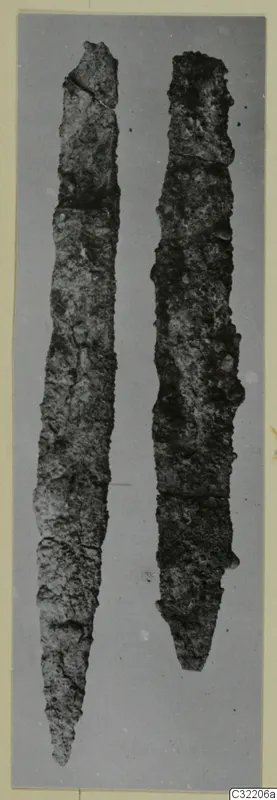 Two long corroded iron tools laid side by side on a plain grey background.