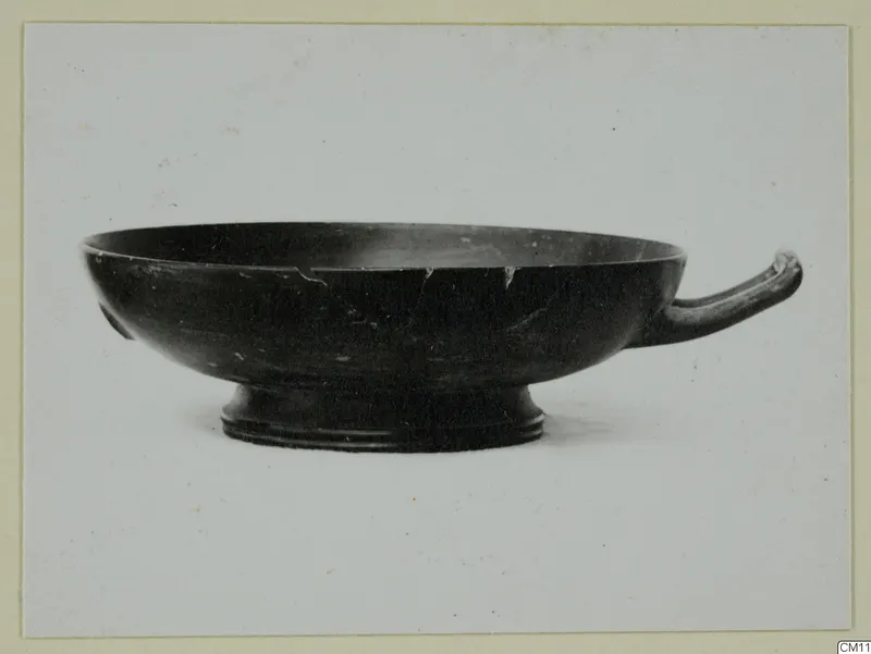 Black-glazed bowl with a single horizontal handle and a low foot, seen from the side.