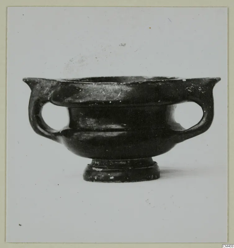 Black glazed pottery bowl with two loop handles and a short foot, seen from the side