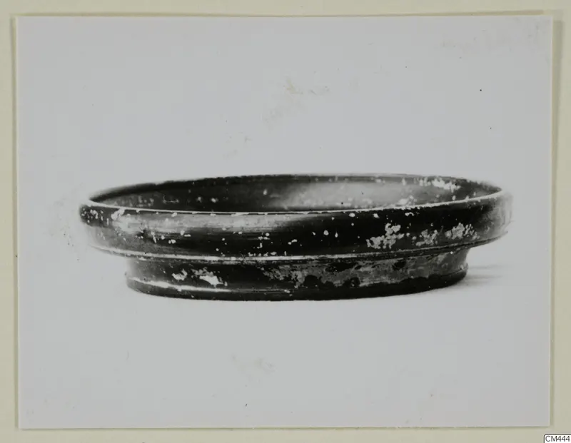 Shallow black-glazed bowl with a low ring foot, seen from the side against a pale background.
