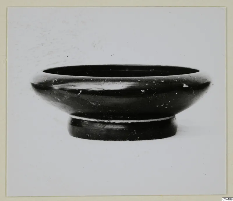 Black-glazed bowl with a wide, rounded rim and a low foot, photographed against a plain background.