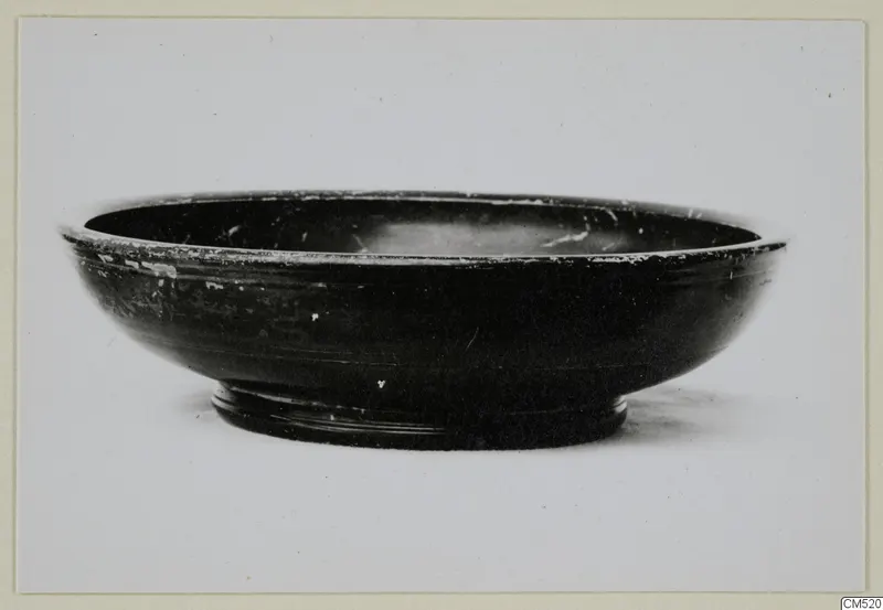 Black-glazed bowl with a ring foot and a chipped rim, photographed against a plain background