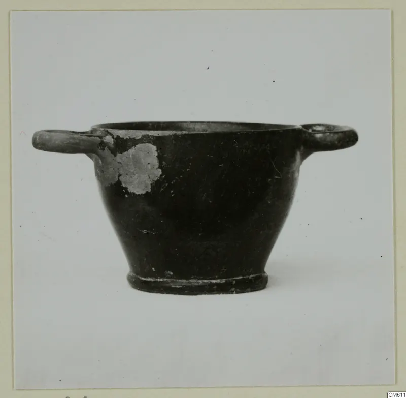 Black-glazed pottery bowl with two horizontal handles, photographed against a plain background.