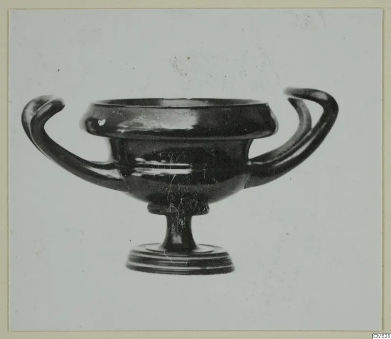 Black-glazed pottery bowl with two horizontal handles and a low foot, photographed against a plain background.