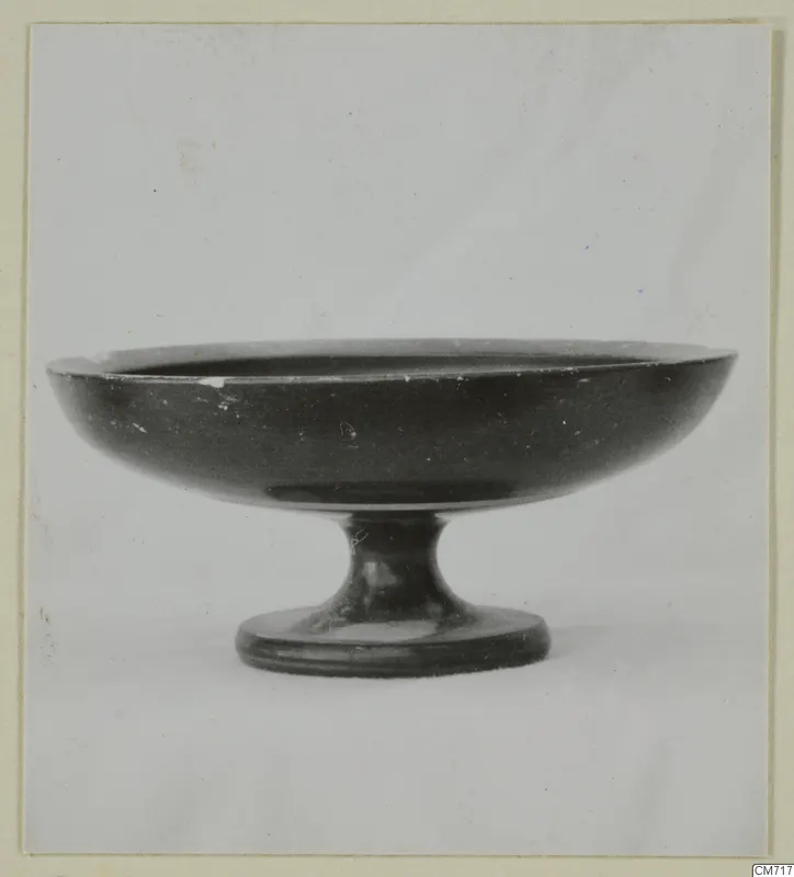 Black-glazed pedestal bowl with a wide, shallow bowl on a short stem and round foot, photographed against a plain background.