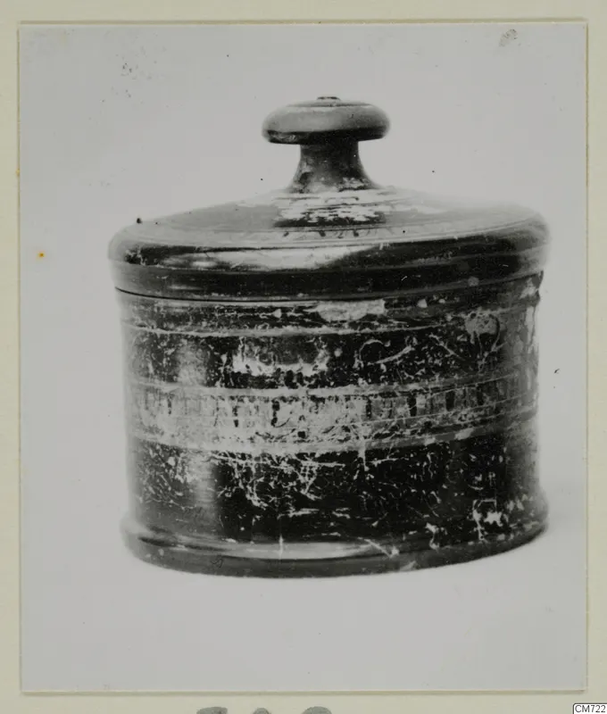 Lidded cylindrical pottery vessel with a knob handle on its lid and a worn dark surface with pale bands