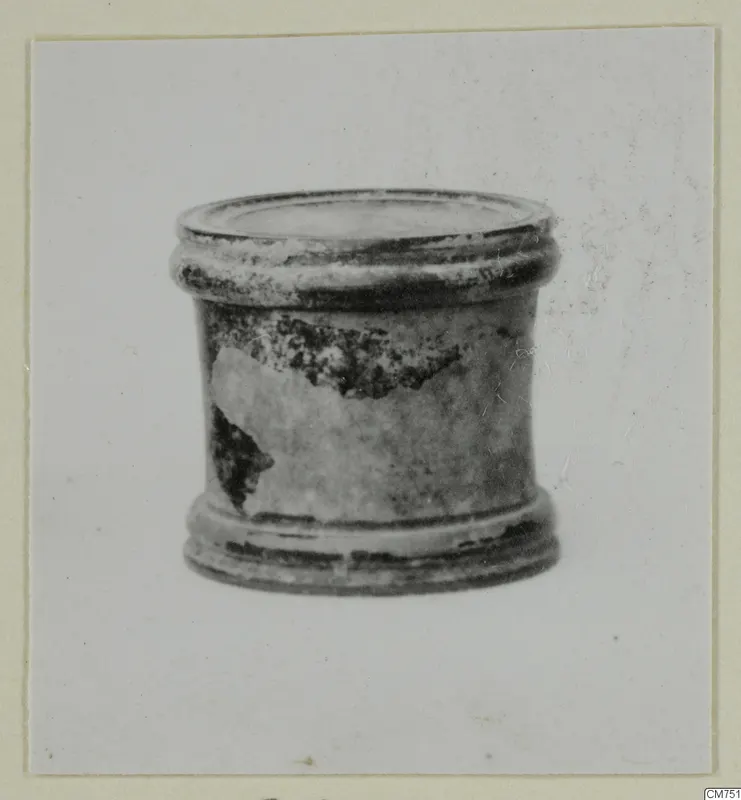 Small cylindrical vessel with a ridged rim and base and a dark, flaking glaze, shown against a plain background