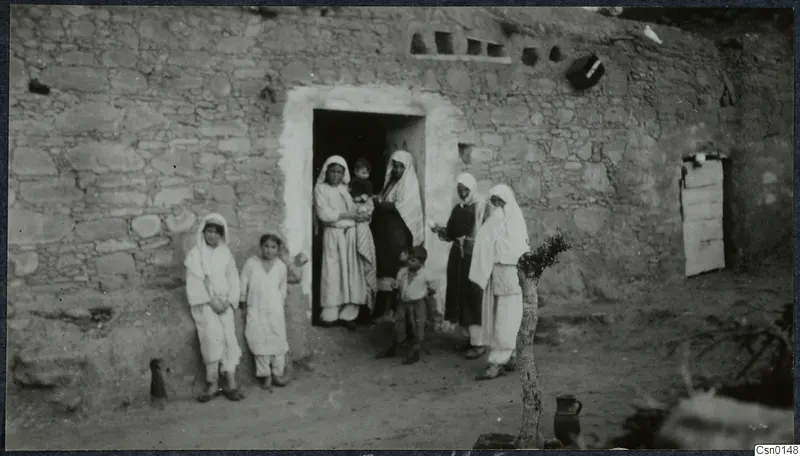 Women, children and a small boy grouped at the doorway of a stone house, probably a village in the Karpas peninsula