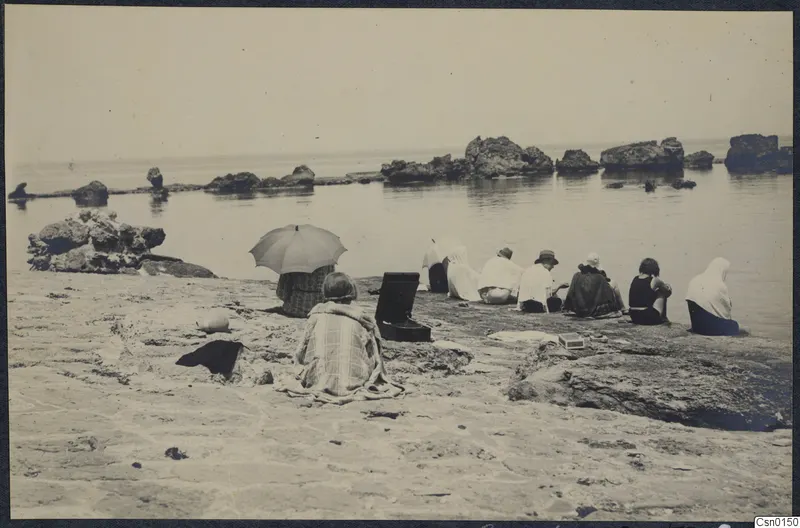 Expedition members seated on a rocky beach below Vouni, facing the sea