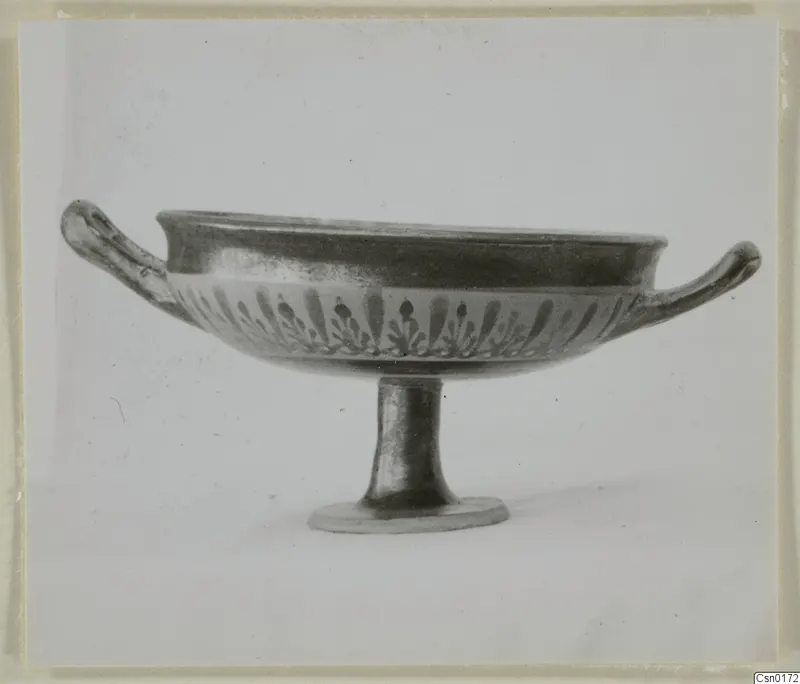Black-glazed bowl on a tall foot, with two horizontal handles and a band of leaf-like motifs below the rim