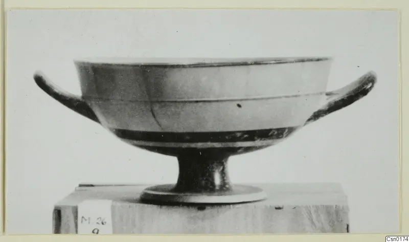 Two-handled footed bowl with dark glaze bands, shown in side view on a wooden block.