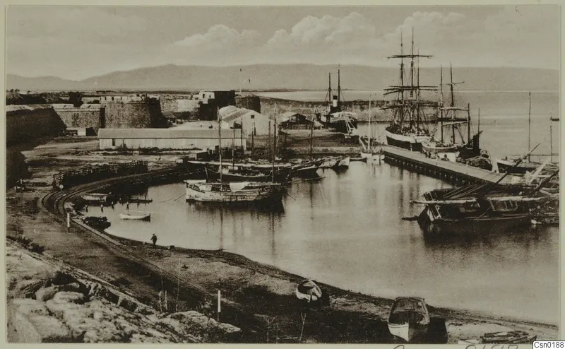 Harbour at Famagusta with moored sailing boats, a masted ship at a jetty and a stone fortification wall.