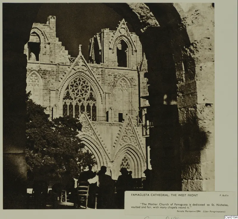West front of Famagusta cathedral with a round window, seen past a tree and silhouetted people.