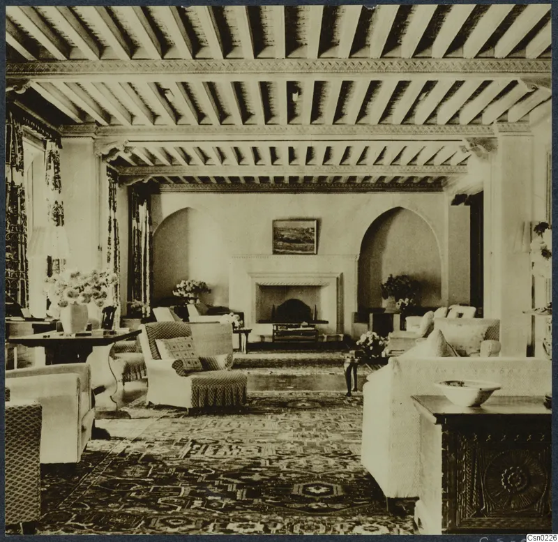 Furnished room in Nicosia with a beamed timber ceiling, arched alcoves, a fireplace, armchairs, a table and a framed picture.