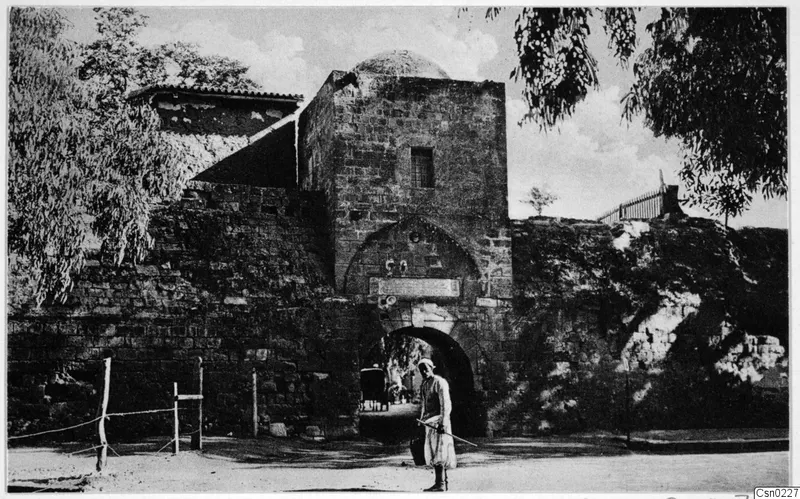 Stone gateway with a domed tower in the city wall at Nicosia, with a standing man in light clothing in front.