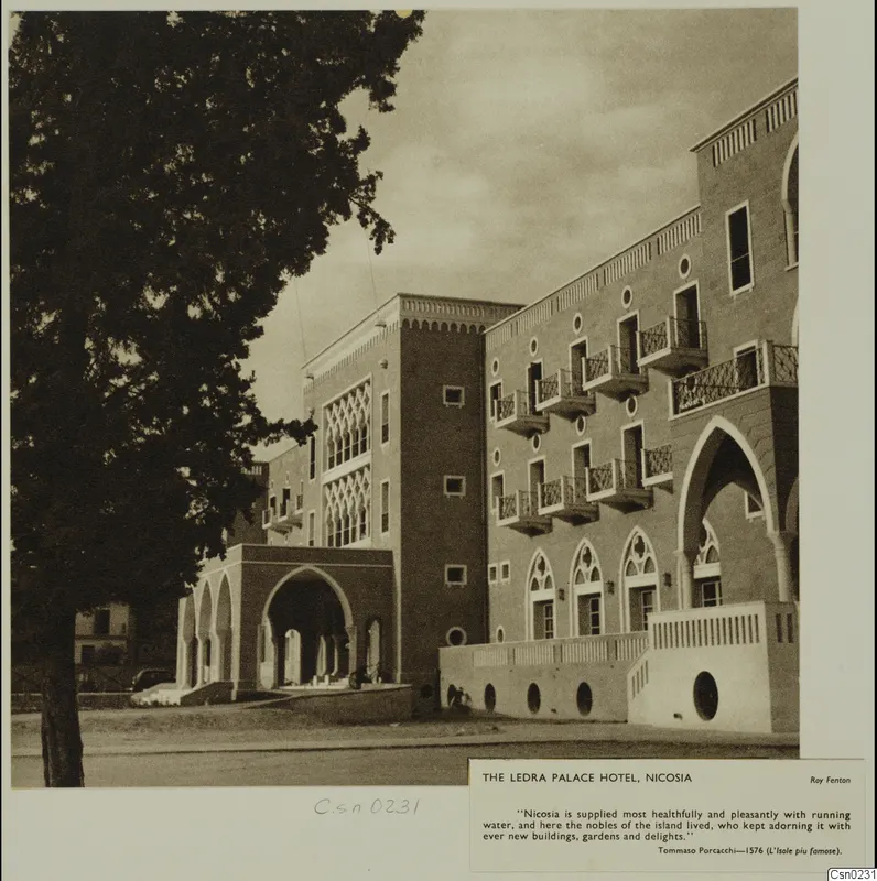 Ledra Palace Hotel, Nicosia, with arched openings and balconies, seen beside a large tree in the foreground.