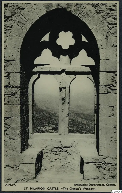 Pointed stone window with carved tracery, looking out over hills and scrubby vegetation in the Kyrenia Mountains.