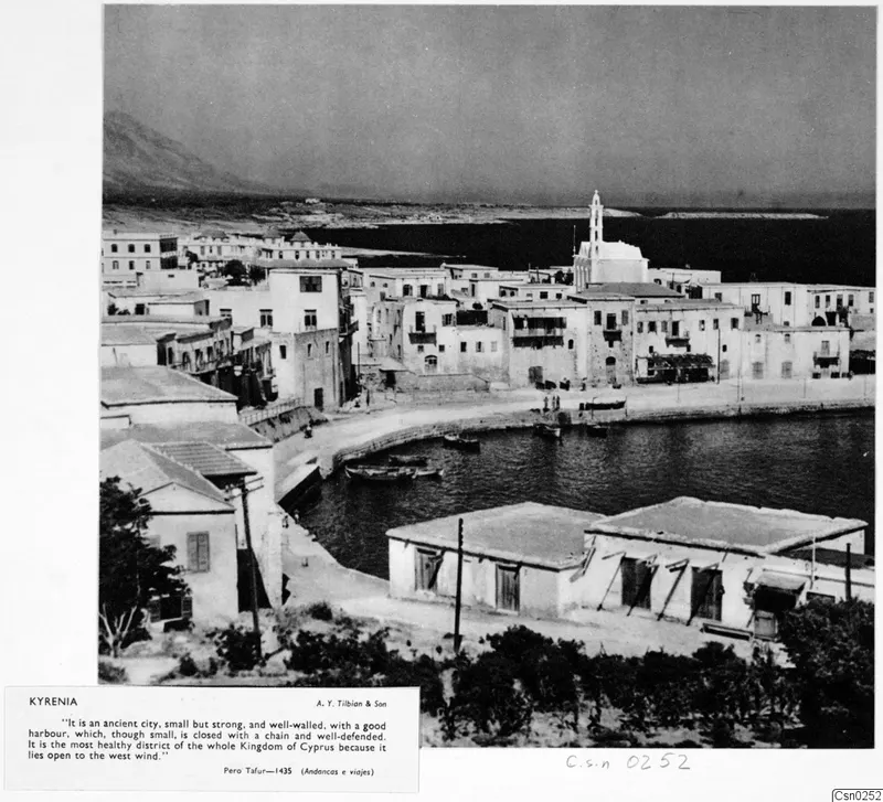 Kyrenia harbour with a curved quay, white houses, moored boats and a white tower above the town