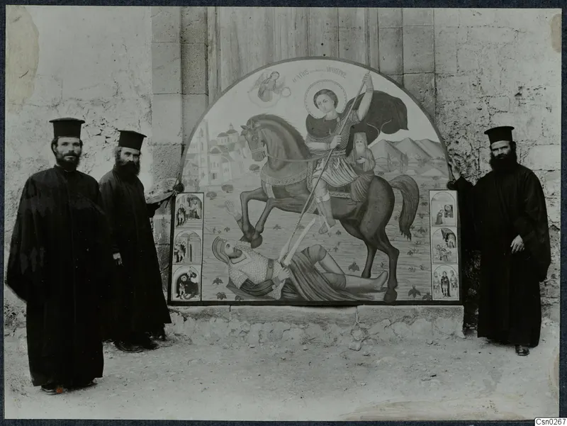 Three bearded men in black robes and tall black hats stand beside a large arched painted panel of a mounted rider with a spear.
