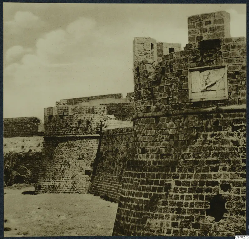 Thick stone fortification wall with square towers and a carved relief panel set into one tower face