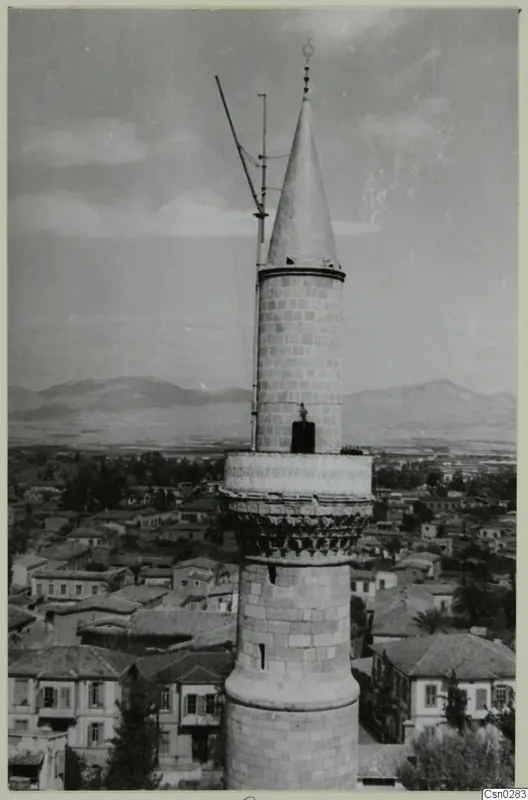 Tall stone tower with a conical cap rising above the rooftops of Nicosia, with mountains beyond.