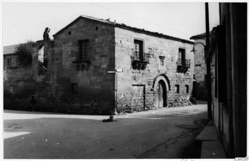 Stone building with an arched wooden doorway and iron balconies on a street in Nicosia, with a dog lying in the road.