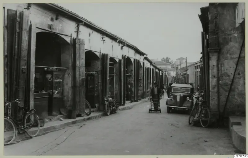 Street in Nicosia lined with arcaded shops, with a parked car, bicycles and people in the roadway.