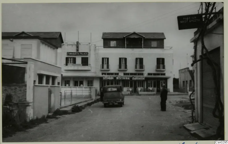 Street at Salamis, Famagusta, with a parked car, white multi-storey buildings and one standing person.