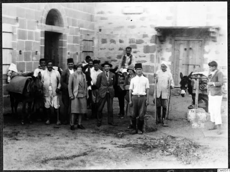 Group of people and two donkeys in a courtyard in front of a stone building with an arched doorway