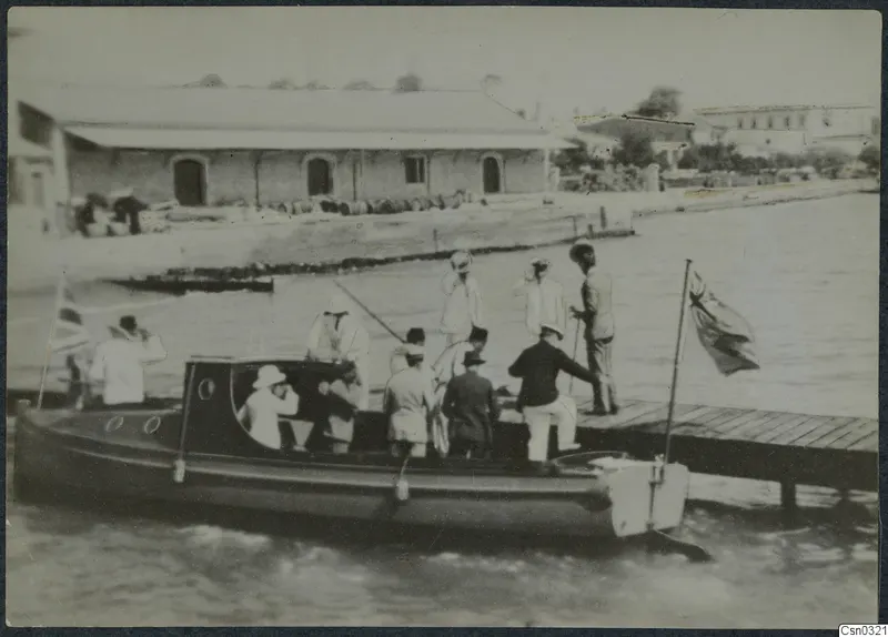 Group of men and a woman in hats on a motor launch alongside a wooden jetty at Limassol
