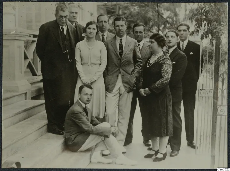 Group of ten people posed on the front steps of the Pierides house in Larnaca, beside an iron gate.