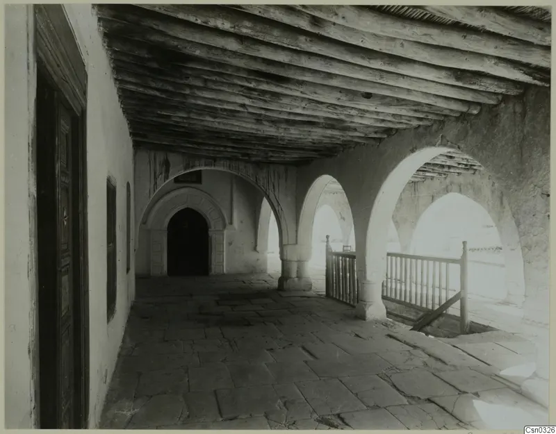 Covered arcaded gallery of a monastery building at Bellapais, with a timber ceiling, a wooden door and a railed stair
