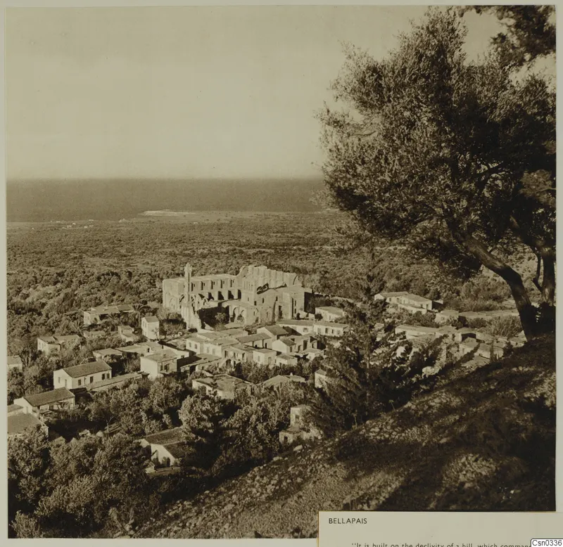 Hillside village of Bellapais with a large ruined church among houses and trees, with the plain and sea beyond