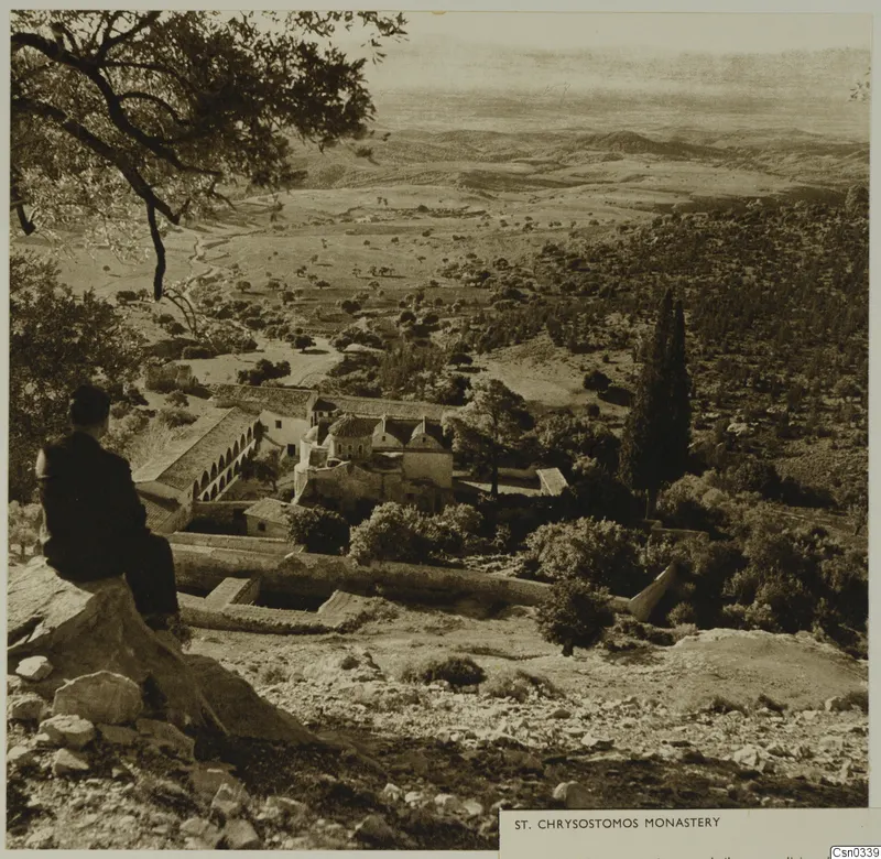 St Chrysostomos Monastery seen from a rocky hillside, with a seated man in the foreground