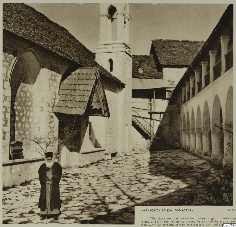Courtyard of Khrysoroyiatissa Monastery with a stone bell tower, an arcaded gallery and a bearded man holding a staff