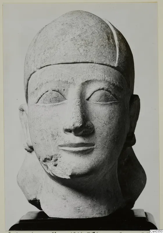 Limestone head of a statue with a close-fitting cap, shown frontally on a dark wooden base