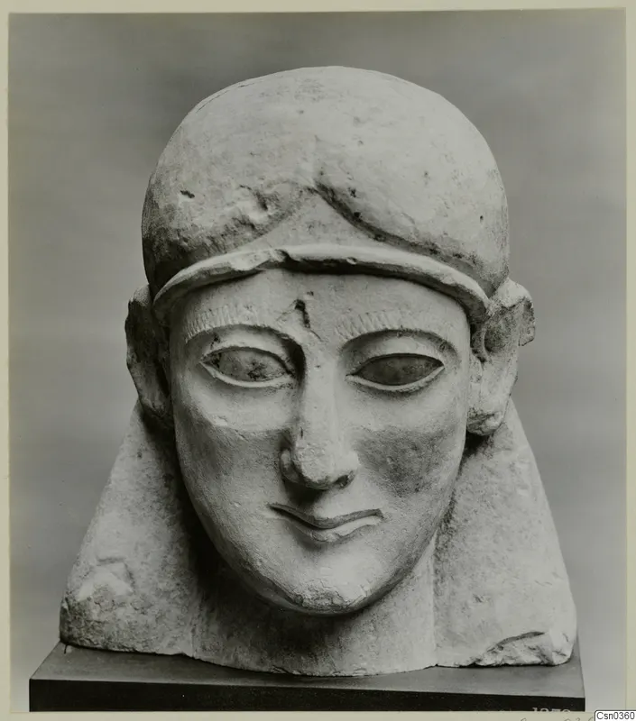 Limestone sculpted head of a figure wearing a close-fitting cap, with a smiling mouth and almond-shaped eyes.