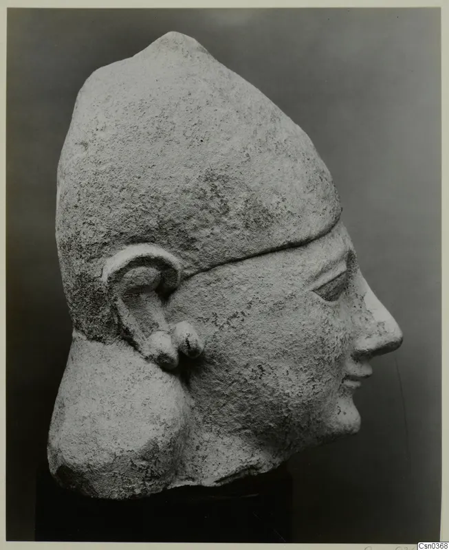 Limestone head in profile wearing a tall cap-like headdress, with a rough, weathered surface