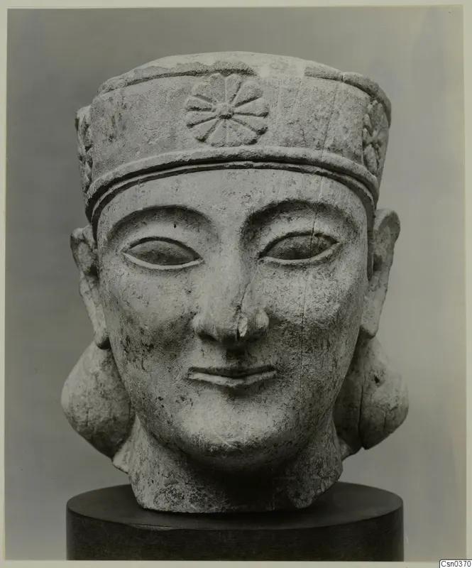 Limestone Neo-Cypriote head sculpture with a tall cylindrical headdress, shown on a dark stand