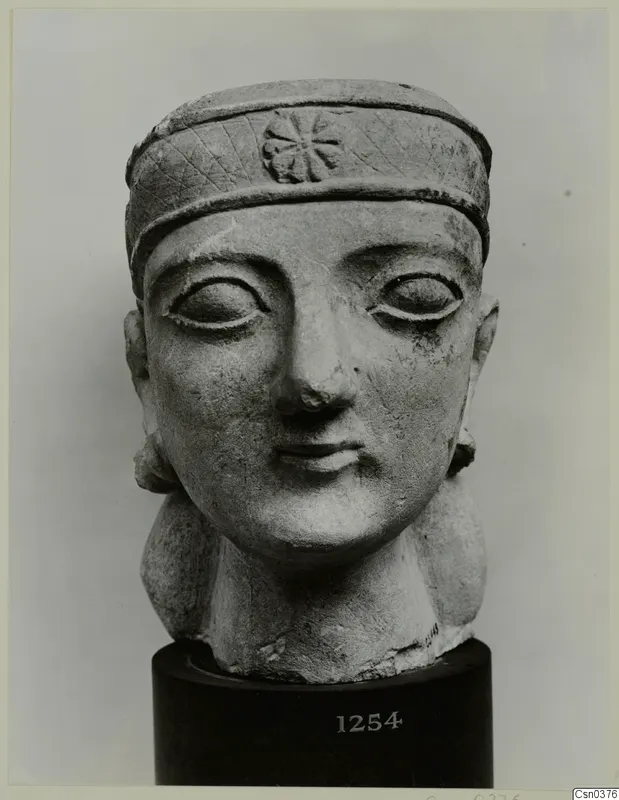 Limestone Neo-Cypriote head of a figure wearing a headband, shown on a dark cylindrical stand