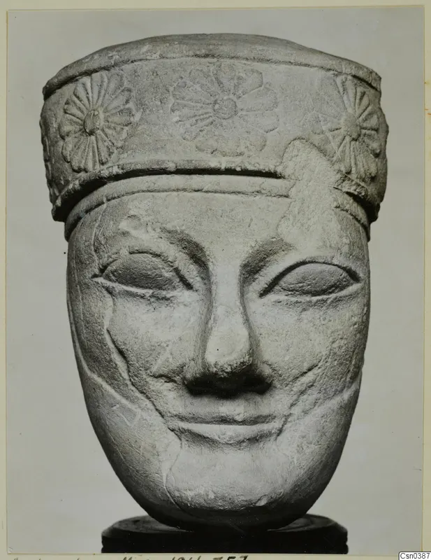 Limestone head with a carved band of rosette-like flowers around its top, seen from the front