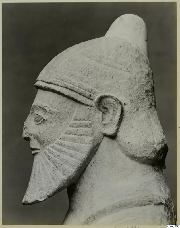 Limestone sculpture of a bearded head in side profile, wearing a tall cylindrical cap