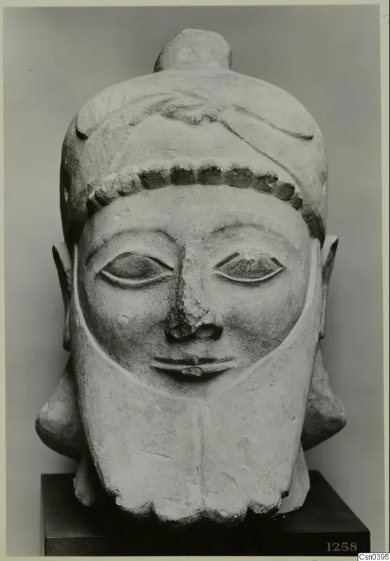 Carved limestone head of a bearded figure with a bead band and a hair knot