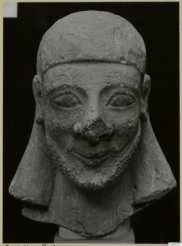 Limestone head sculpture with a smiling face and short beard, shown from the front.