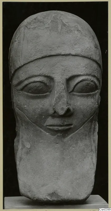 Carved limestone head sculpture with a close-fitting cap, large eyes and a straight nose, shown against a black background.