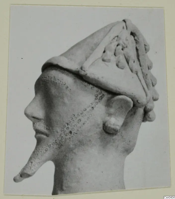 Terracotta head in profile with a tall conical headdress, applied ridges and knobs, and a dotted pattern on the cheek
