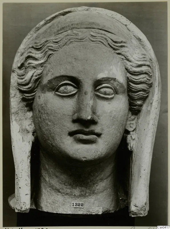 Limestone head of a female figure with wavy hair and a tall veil, photographed frontally against a dark backdrop