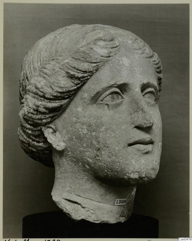 Limestone head of a woman with wavy hair combed back from the face.